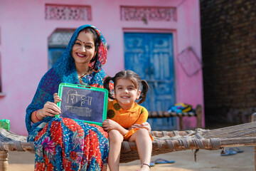 education concept : Indian rural woman showing shiksha words in hindi calligraphy with daughter