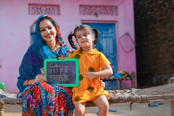 education concept : Indian rural woman showing shiksha words in hindi calligraphy with daughter