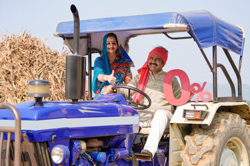 Indian farmer sitting with wife on tractor and showing zero percent board at field.