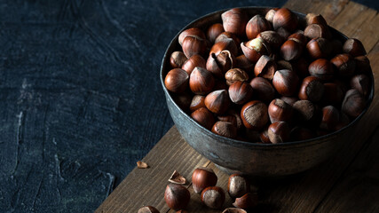 Shelled hazelnuts in metal bowl on wooden background in rustic style. Copy space. 