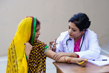 Indian woman doctor injecting to rural woman at clinic - obrazy, fototapety, plakaty