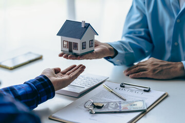 Fototapeta na wymiar House purchase concept, real estate agent with house model talking to client about buying home insurance and client signing contract under formal contract agreement with real estate law