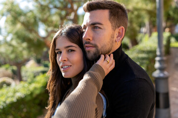 Young woman in sweater touching beard of boyfriend on blurred background of park on Saint Valentine Day