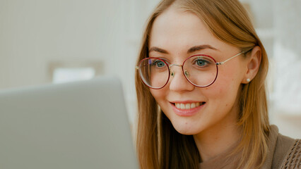 Close up Caucasian woman female face girl in glasses eyes look at laptop screen. Freelancer smiling...