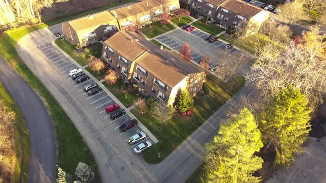 Flying over a large three story barn style house apartment complex with outdoor parking and colorful fall foliage in early morning light in Penfield, New York, USA. Suburban parkside rental units