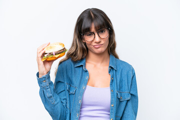 Young caucasian woman holding a burger isolated on white background with sad expression