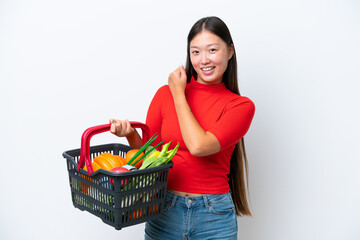 Obraz na płótnie Canvas Young Asian woman holding a shopping basket full of food isolated on white background celebrating a victory