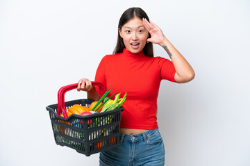 Obraz na płótnie Canvas Young Asian woman holding a shopping basket full of food isolated on white background with surprise expression