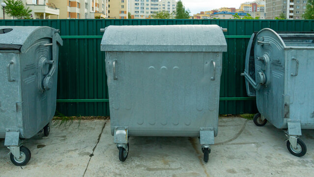 Modern metal containers for separate garbage collection. Garbage cans in the city on the background of a house. Environmental disaster, problems of waste removal, collection and disposal in a big city