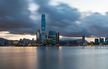 Obraz na płótnie Canvas As the sun rises. Long exposure of the early morning clouds over buildings in Kowloon, Hong Kong. Silky smooth sea in the foreground.