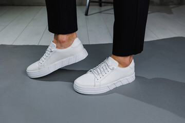 Close up of male legs in black pants and white casual sneakers. Men's leather summer shoes