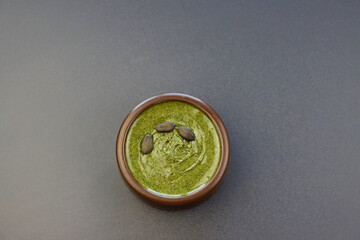 Green pumpkin seed paste in a brown round bowl on a gray background. 