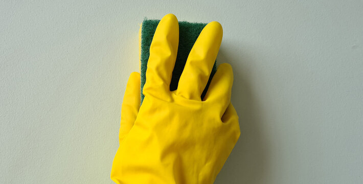 Hand in yellow rubber glove wipes stain on wall with sponge