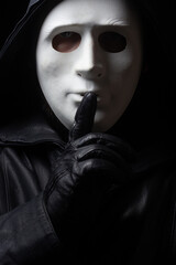 Man in terrible face mask staring at camera against dark background cloak with hood