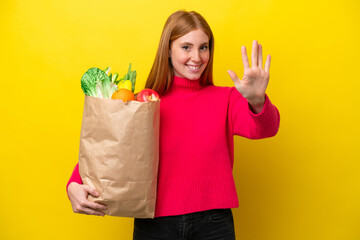 Young redhead woman holding a grocery shopping bag isolated on yellow background counting five with fingers