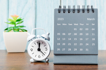 The March 2023 Monthly desk calendar for 2023 year with alarm clock on blue wooden background.