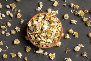 Dry chamomile in a small bowl and scattered chamomile on table, top view. Healthy herbal tea.