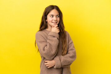 Little caucasian girl isolated on yellow background thinking an idea while looking up