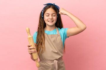 Little caucasian girl holding a rolling pin isolated on pink background doing strong gesture
