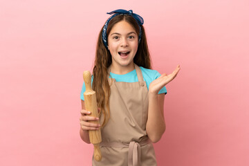 Little caucasian girl holding a rolling pin isolated on pink background with shocked facial...