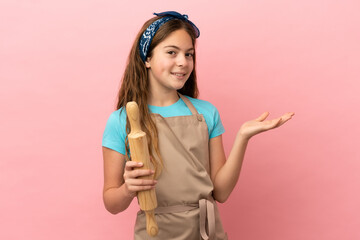 Little caucasian girl holding a rolling pin isolated on pink background extending hands to the side for inviting to come