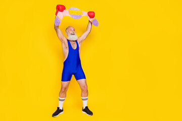 Fototapeta na wymiar Full size portrait of cheerful funky grandfather arms boxing gloves hold champion belt empty space isolated on yellow color background