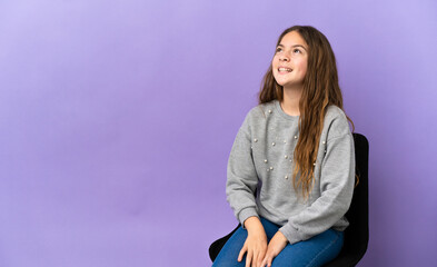 Little caucasian girl sitting on a chair isolated on purple background laughing