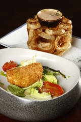 Deep fried breaded cheese with vegetables and tomatoes and onion rings tower