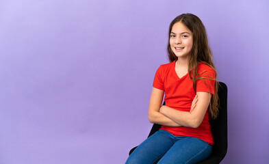 Little caucasian girl sitting on a chair isolated on purple background with arms crossed and looking forward