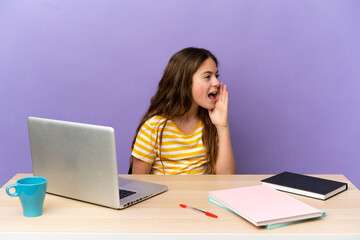 Little student girl in a workplace with a laptop isolated on purple background shouting with mouth wide open to the side