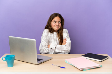 Little student girl in a workplace with a laptop isolated on purple background making doubts gesture while lifting the shoulders