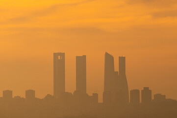 Fototapeta na wymiar The sun silhouettes the skyscrapers of Madrid known as the 'Four Towers Business Area' during a day with pollution