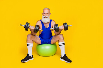 Full body length photo of old aged senior sitting gymnastics ball practicing dumbbells up powerful athlete isolated on yellow color background