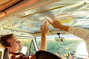 Summer travel concept. cropped friends or couple looking at map to plan a camper van trip pointing finger at map. rear view, view from back. vacation, holidays, adventure, journey, trip, travel