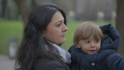 Obraz premium Mother walking outside holding baby toddler in arms, mom kissing son in cheek