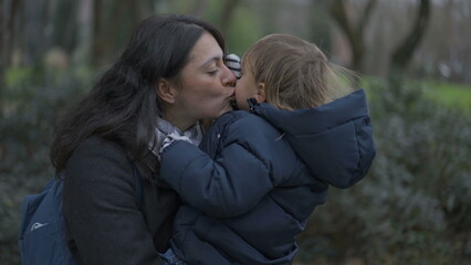 Fototapeta premium Mother and toddler boy walking outside at park. Mom kissing child in cheek