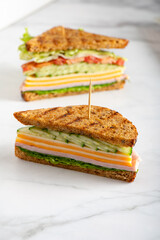 Sliced in middle high closed sandwich with wholemeal bread, cheese, ham, tomatoes, cucumber and letuce salad leaves