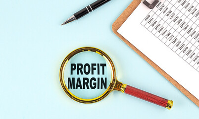 PROFIT MARGIN text on magnifier with clpboard on blue background