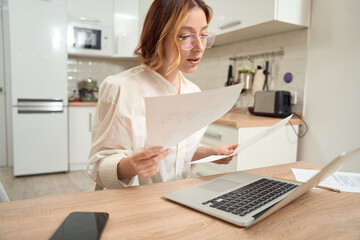 Concentrated lady with papers sitting at portable computer