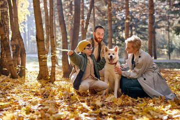 happy family with dog on walk in autumn park. family, pet, domestic animal and people concept. young man, woman and child boy in coats outdoors on warm weather. human emotions concept
