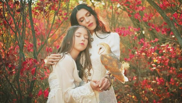 Two fantasy women walking in forest, young mother and adult daughter. Vintage dress. Owl barn owl white bird sits on hand Wisdom sign symbol. Woman queen and little girl princess. Autumn nature trees