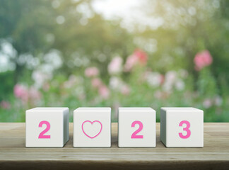 Love icon with 2023 letter on white block cubes on wooden table over blur pink flower and tree in garden, Happy new year 2023 and Valentines day concept