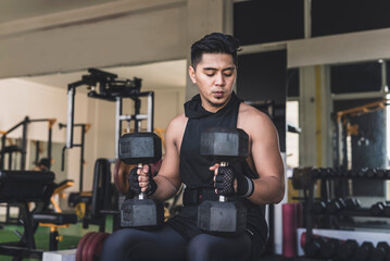 An asian man mentally preparing himself while sitting on an incline bench holding two dumbbells...