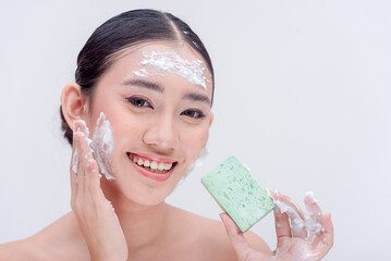 Beautiful Asian young woman practicing proper hygiene by washing her face with a bar of facial...