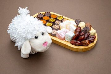 Fototapeta na wymiar Festive harvest festival background with lamb figurine, wooden tray with dates, candies, sweets, chocolate