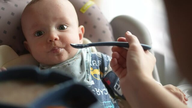 Healthy food. Cute baby boy face. beautiful a baby eats dirty. Healthy food family concept. mother feeds her daughter baby with a spoon, the child is dirty. fun newborn baby breakfast