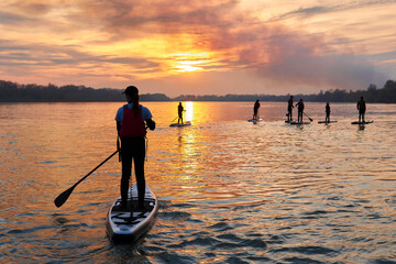 Rear view of a teenagers on stand up paddle board in a river before sunset. View on people paddles...