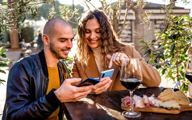Happy couple watching mobile at winery bar - Woman and man sitting outside while smiling looking at...
