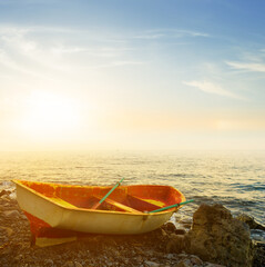 small oared boat on stony sea coast at the sunset