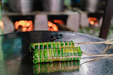 Making (wrapping) Tet Cake (Bánh Tét), the Vietnamese lunar new year Tet food outdoor with old woman hands and ingredients. Closed-up.